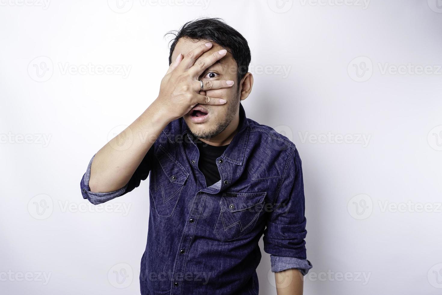 Funny obvious peeking Asian man in blue shirt isolated on white background. photo