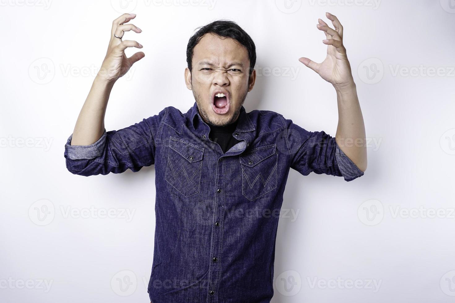 The angry and mad face of Asian man in blue shirt isolated white background. photo