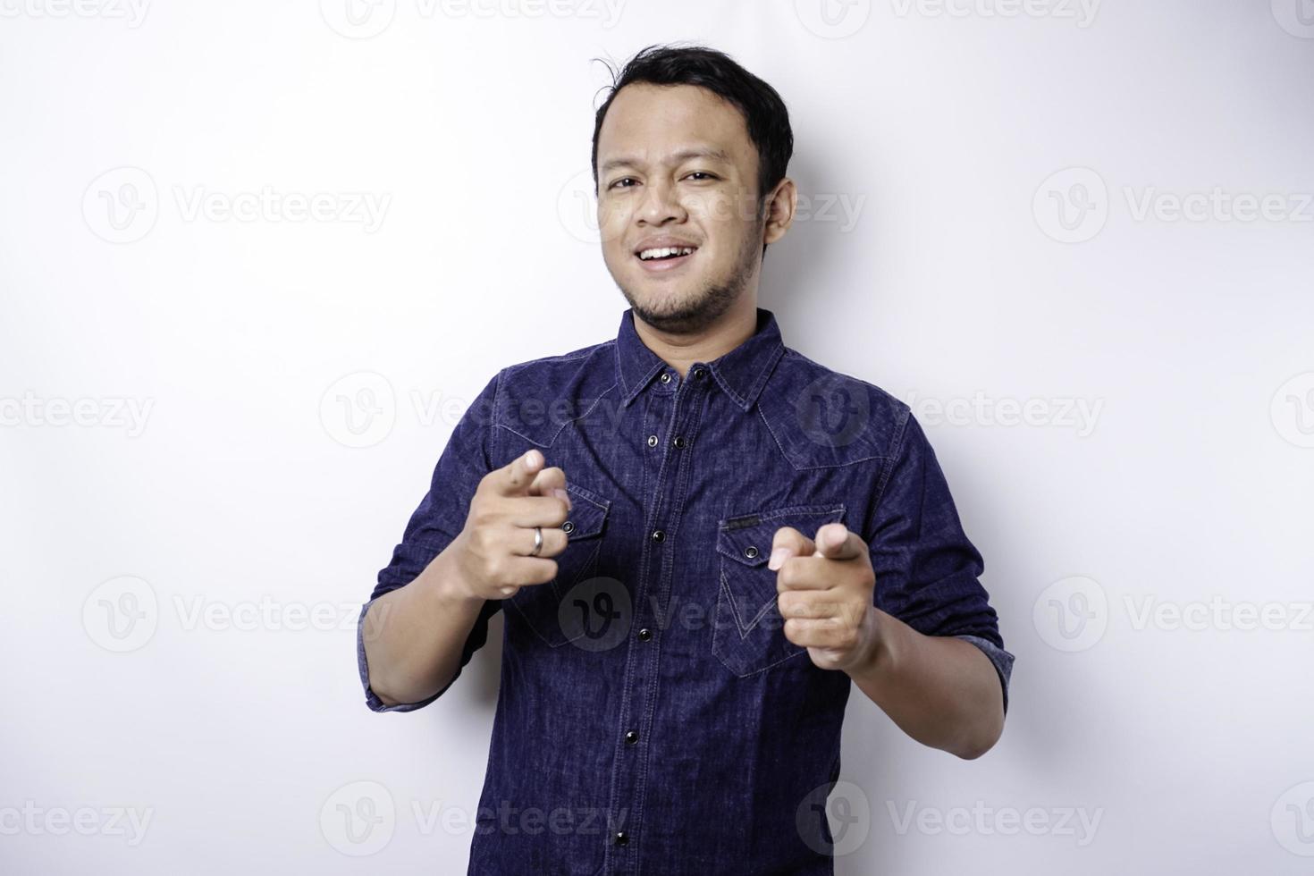 Young Asian man wearing blue shirt standing over isolated white background pointing fingers to camera with happy face. Good energy and vibes. photo