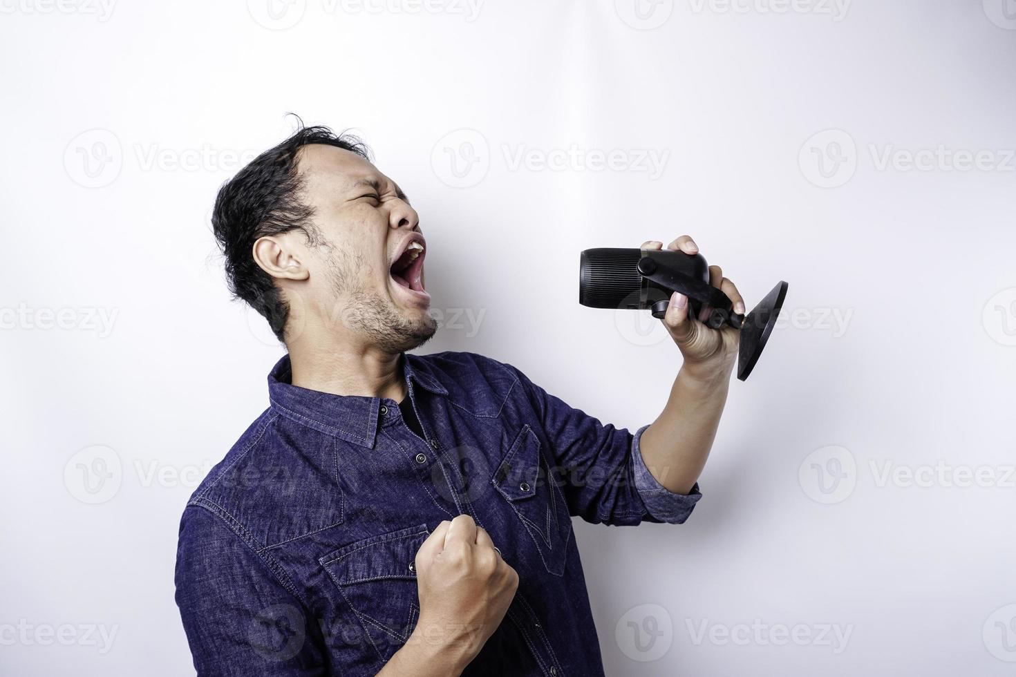 Portrait of carefree Asian man, having fun karaoke, singing in microphone while standing over white background photo