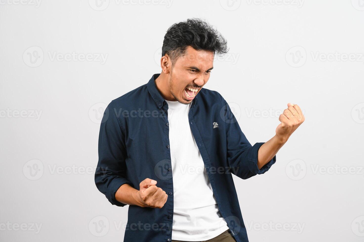 Portrait of Happy young asian man in blue shirt excited doing winner gesture with arm raised isolated on white background photo