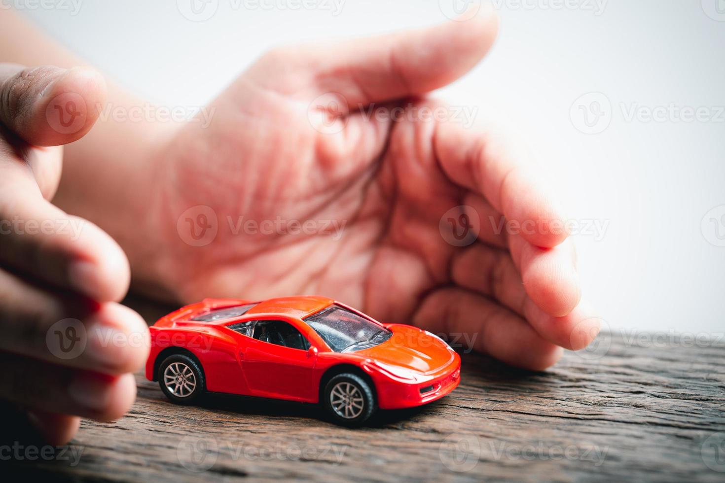Female hands and car as protection of car concept. Woman insurance agent covering toy car on white background, closeup. Hands protecting of car over wooden table. Car insurance and automotive business photo