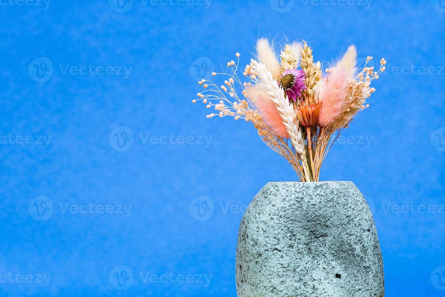 bunch of dry flowers and spikelets in vase on blue photo