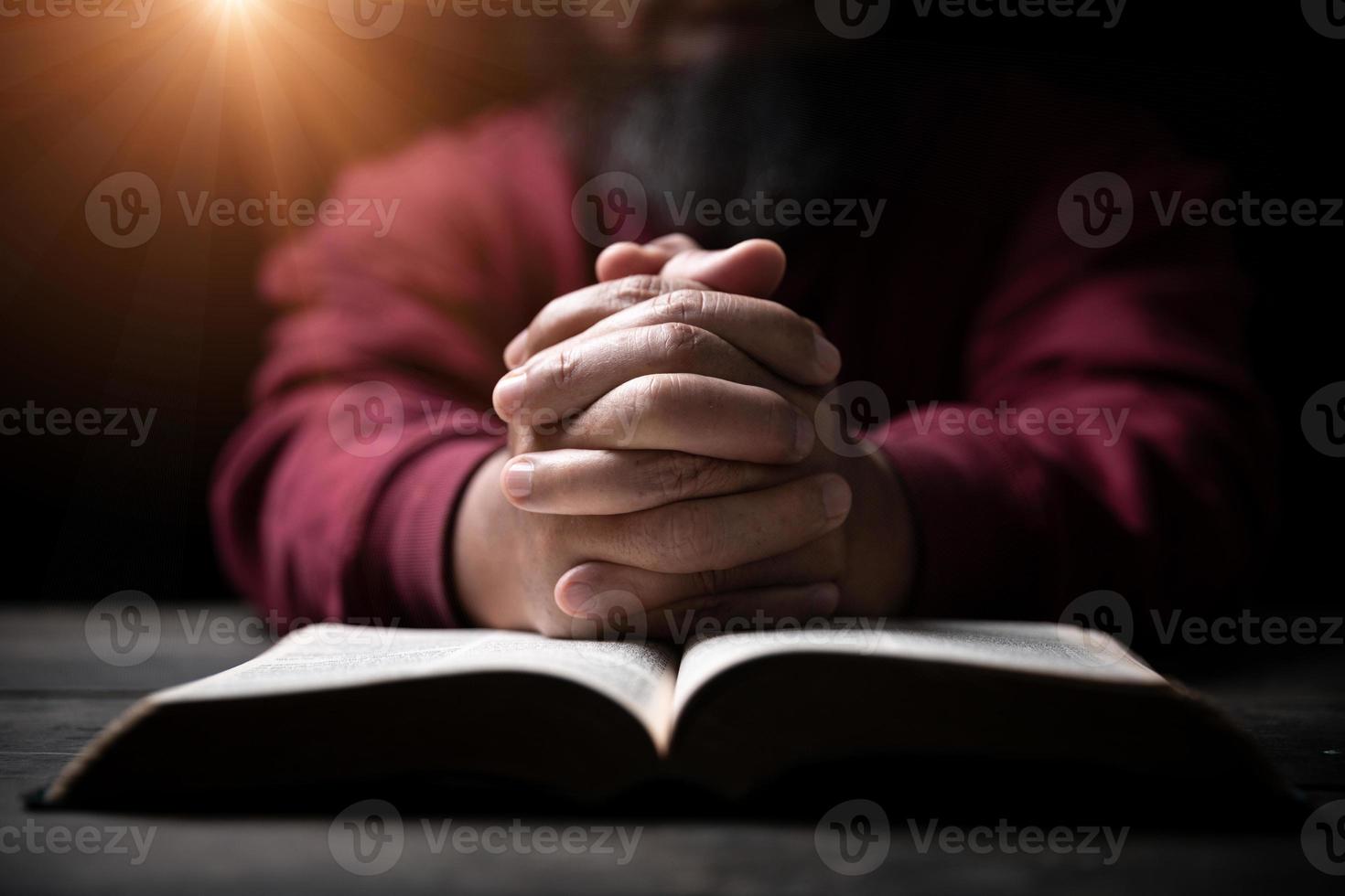 Hands folded in prayer on a Holy Bible in church concept for faith, spirituality and religion, man praying in morning. Man hand with Bible praying. Person Christian who faith in Jesus worship in dark. photo