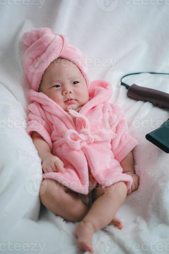 primer plano lindo bebé recién nacido en traje rosa acostado solo en la cama. adorable bebé descansa sobre sábanas blancas, mirando a la cámara con aspecto pacífico. infancia, salud y pediatría, concepto de infancia foto