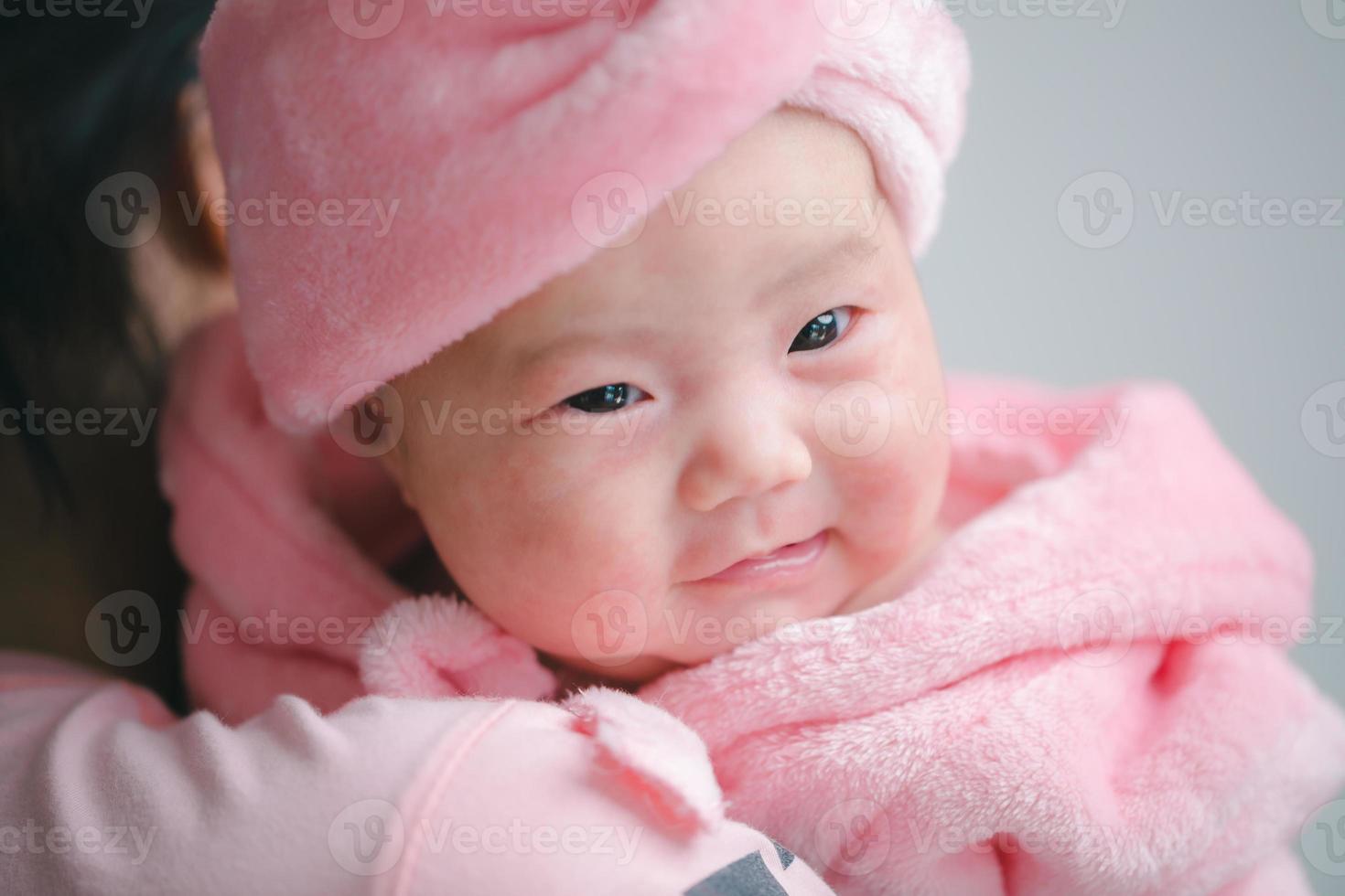 Closeup cute child care with mother indoor. Happy little toddler baby girl smiling lying on bed on white sheet at home looking at camera. Copy space for text. Infancy, healthcare and babyhood concept. photo