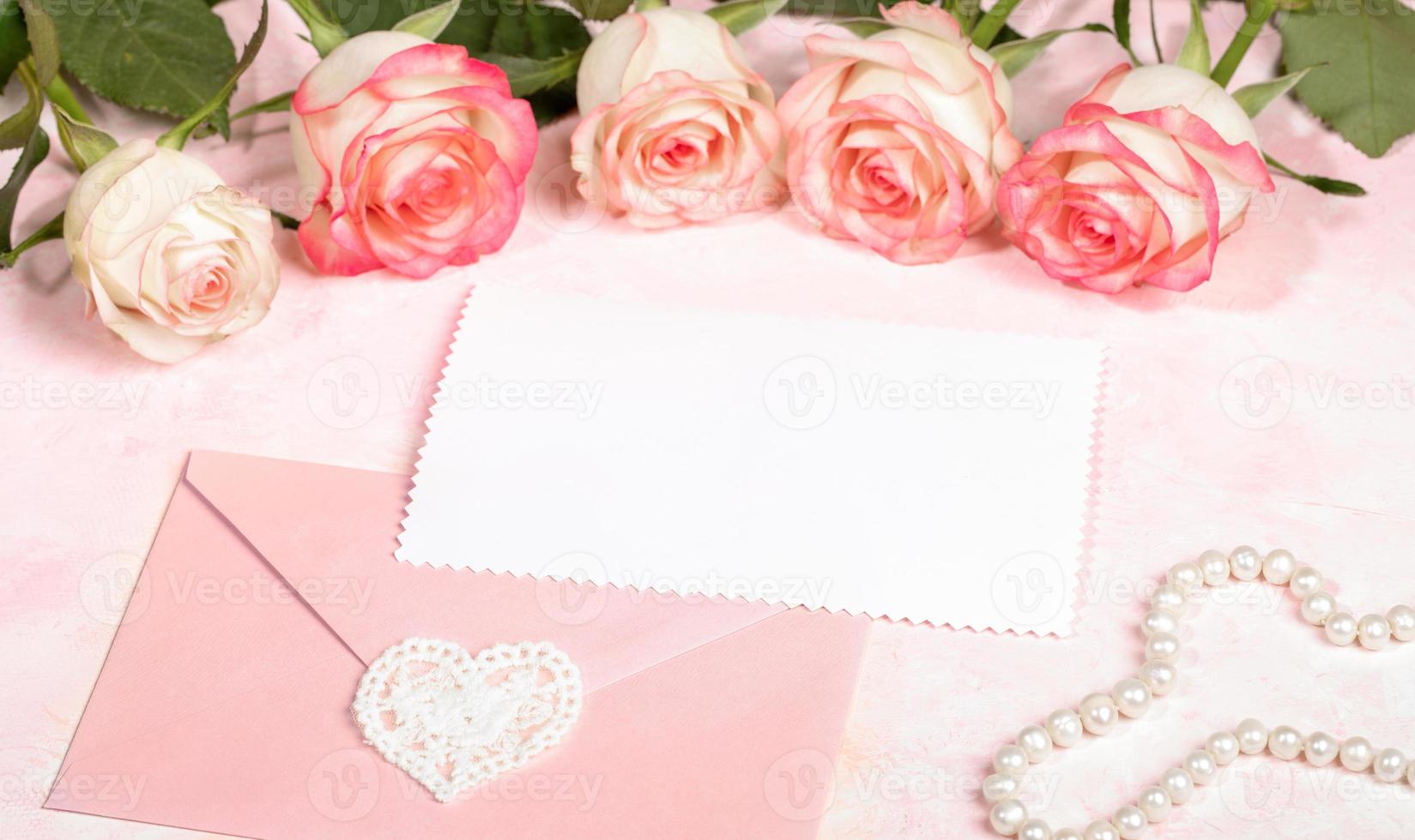 Festive mock up with pink roses, envelope with lace heart, empty white sheet, pearl beads on pink. photo