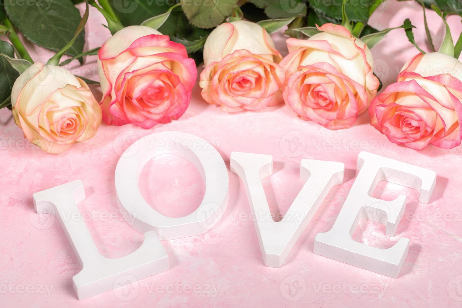 Bouquet of beautiful gentle pale pink roses and white letters LOVE on pink background. Festive card. photo