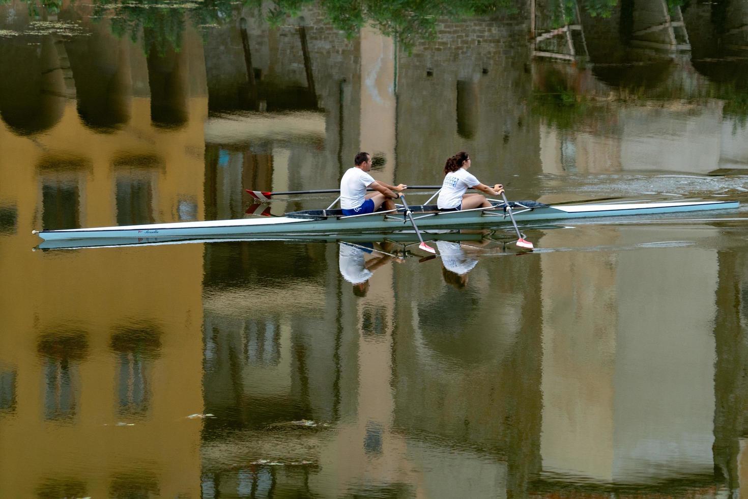 FLORENCE, ITALY - SEPTEMBER 1 2018 - People rowing in town river with old houses reflection photo