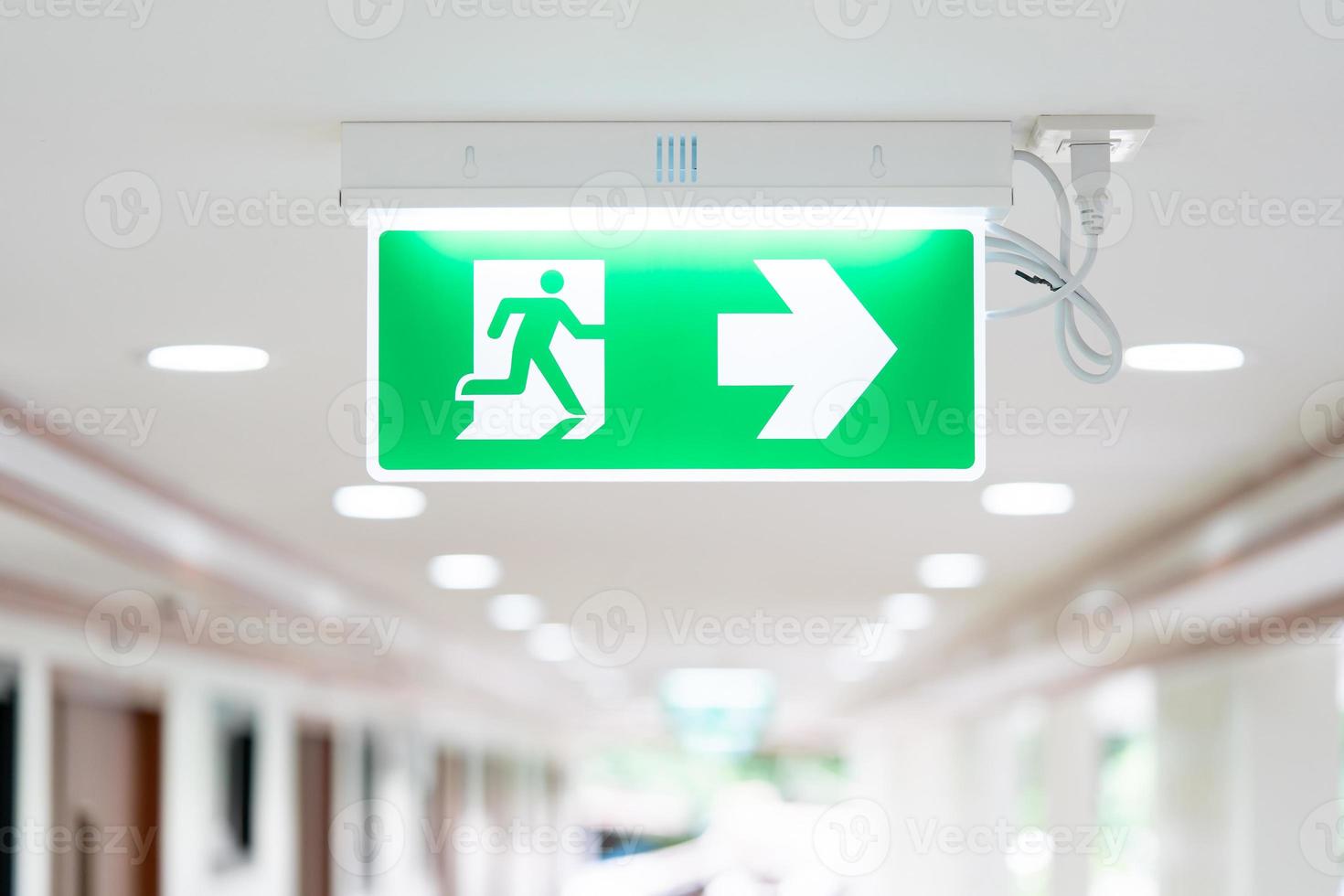 A Arrow light box sign of EMERGENCY FIRE EXIT is hung on the ceiling in hospital walkway, Idea for event fire or evacuation drills. photo