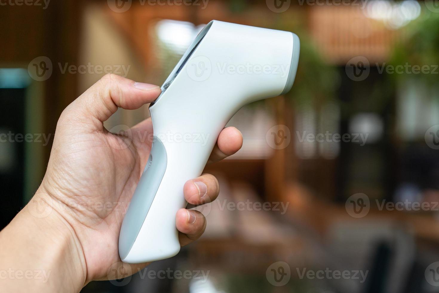 pistola de termómetro en la mano del hombre. es un dispositivo digital de medición de temperatura de la vista infrarroja en una mesa de madera en el campo al aire libre. camino de recortes foto