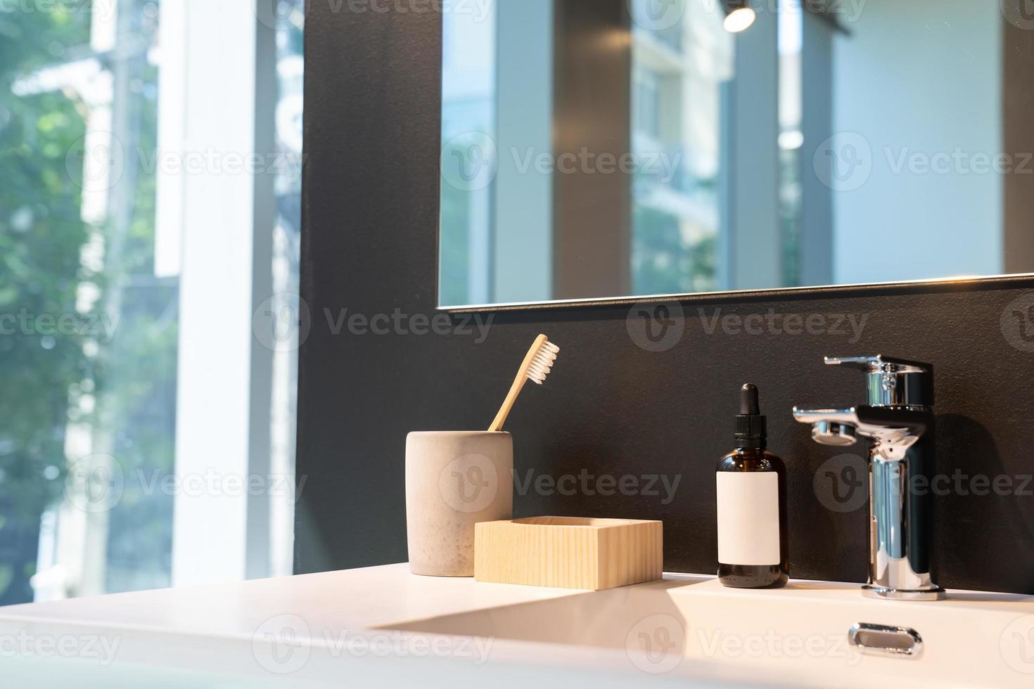 minimal toiletries such as toothbrush, serum bottle and wood storage on white sink and mirror on the black wall. photo