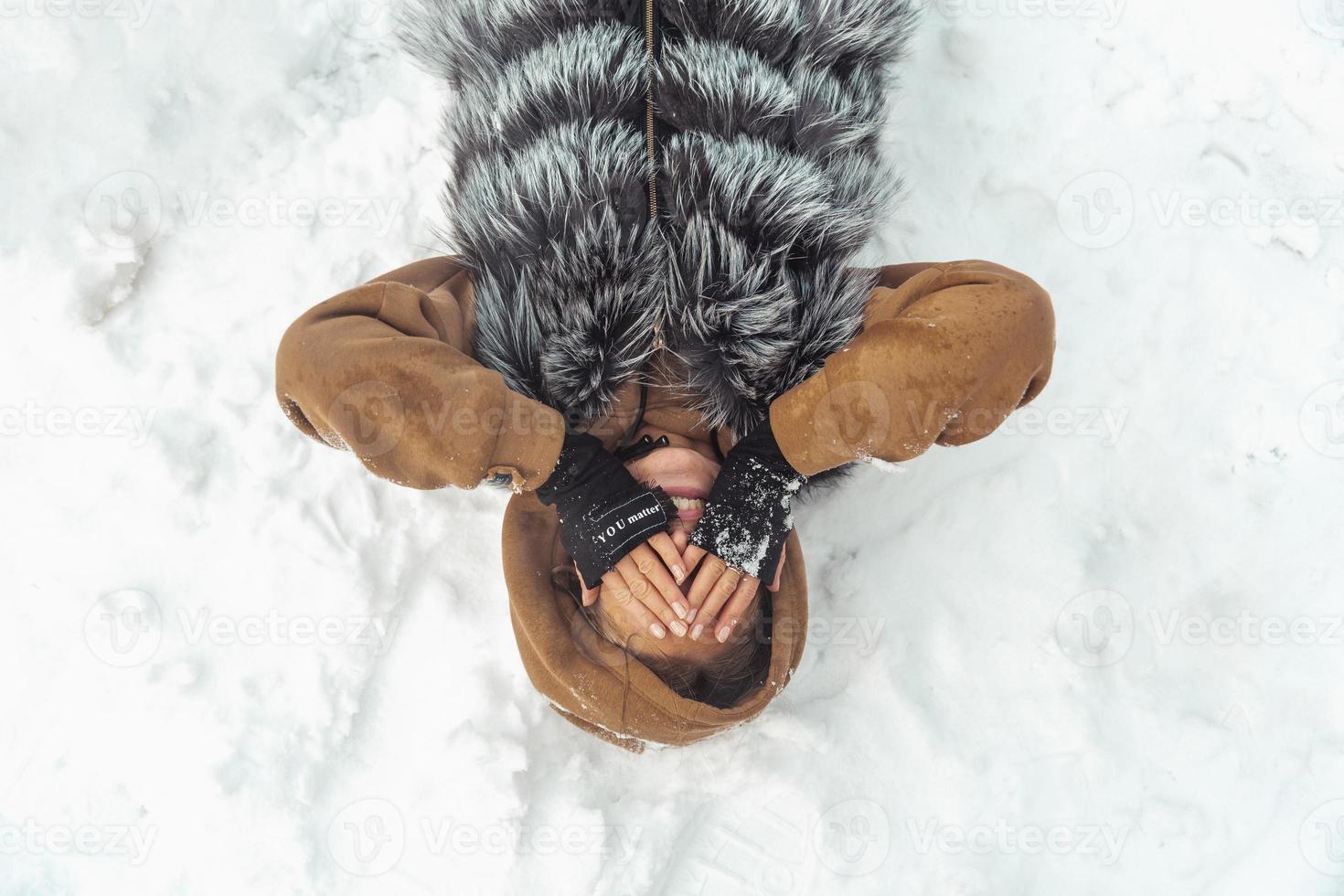 la chica está tirada en la nieve con los ojos cerrados vista desde arriba foto