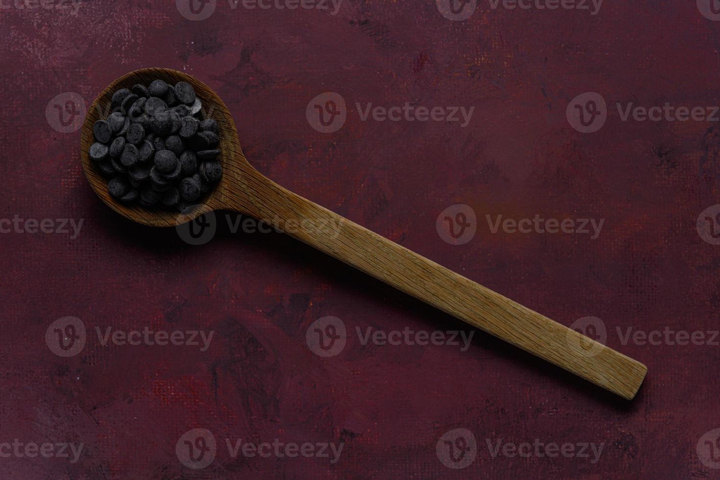 Melt chocolate buttons on wooden spoon on burgundy rustic background photo