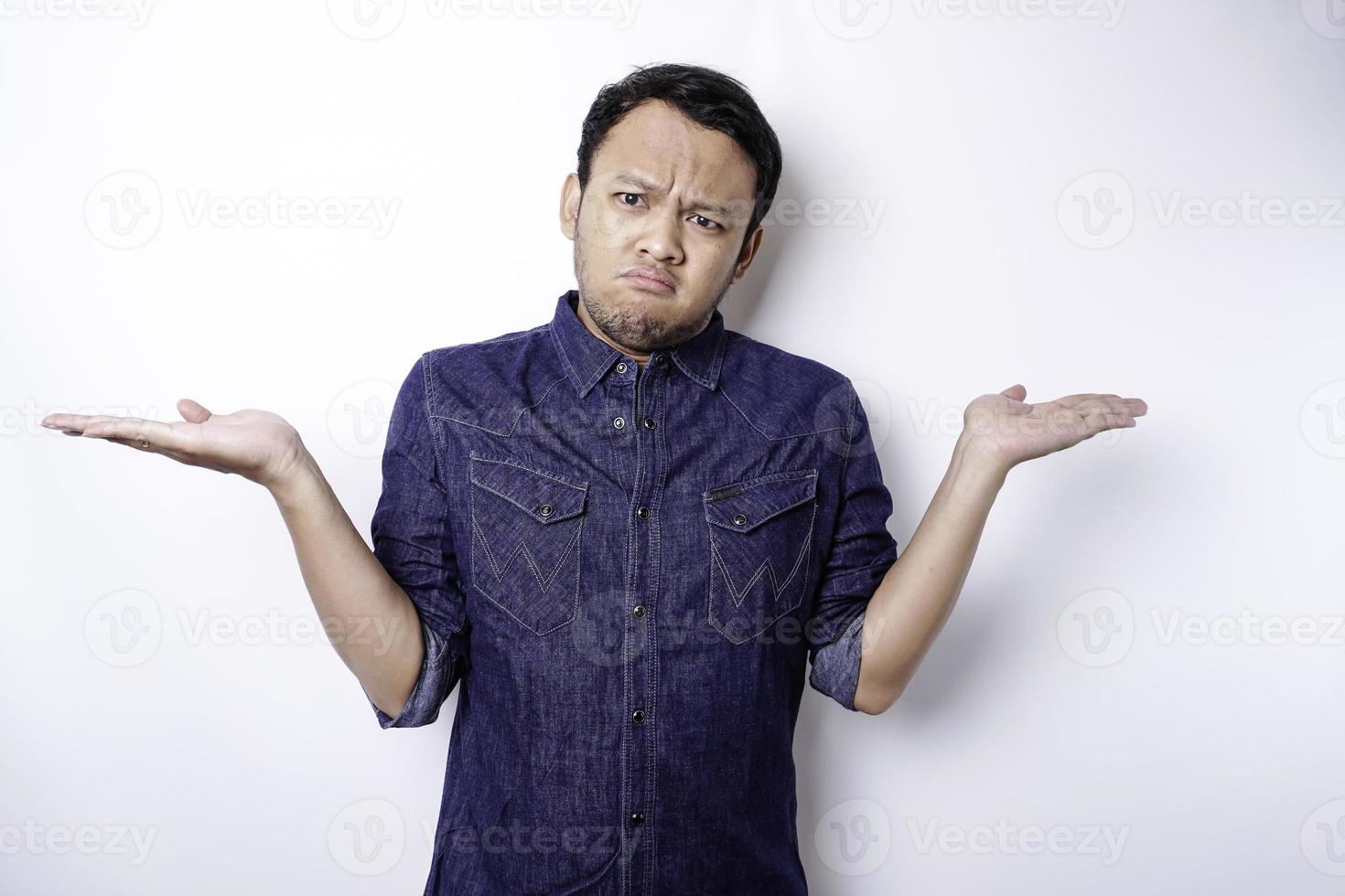 A portrait of an Asian man wearing a blue shirt looks so confused between choices, isolated by a white background photo