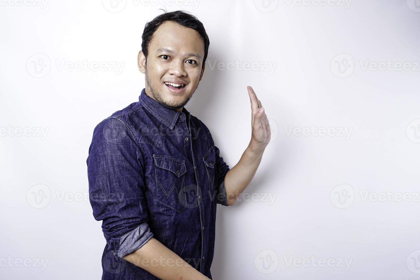 Excited Asian man wearing blue shirt pointing at the copy space beside him, isolated by white background photo