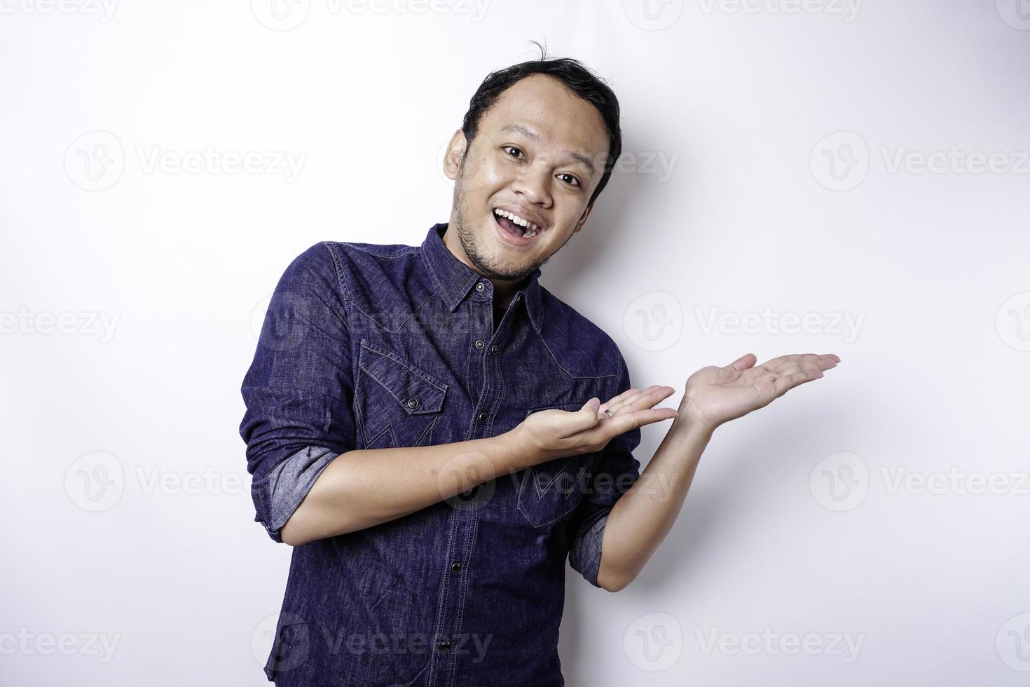 Excited Asian man wearing blue shirt pointing at the copy space beside him, isolated by white background photo