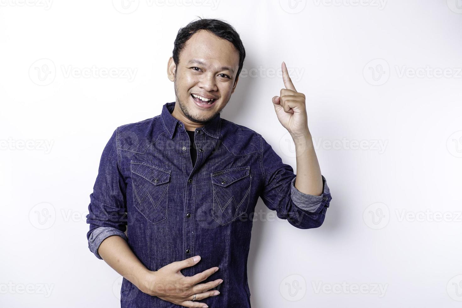 hombre asiático hambriento con pantalones azul apuntando al espacio de copia encima de él, aislado por fondo blanco foto