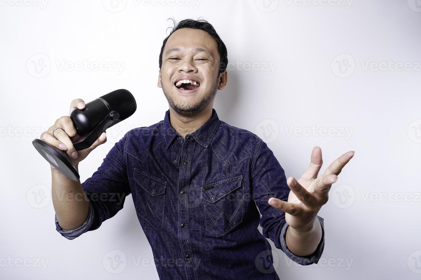 retrato de un hombre asiático despreocupado, divirtiéndose en el karaoke, cantando en el micrófono mientras está de pie sobre fondo blanco foto
