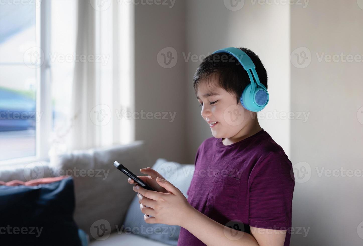 niño de escuela primaria que usa teléfono móvil para buscar información en Internet para la tarea, niño que usa auriculares que estudia en línea con el maestro, educación en el hogar, educación de aprendizaje electrónico, niños con tecnología foto