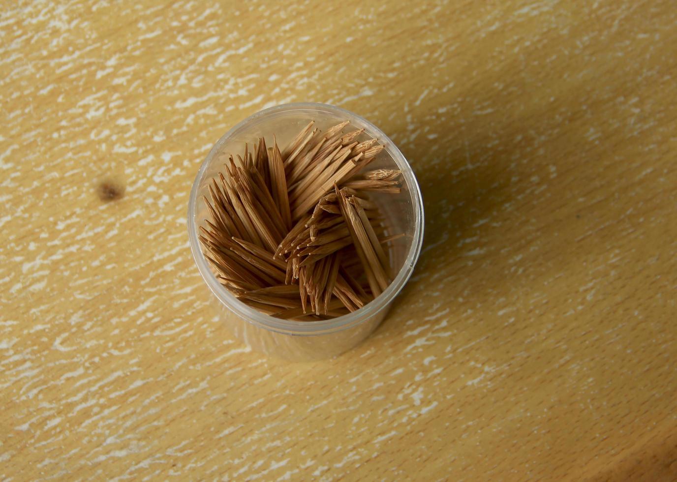 A bunch of wooden toothpicks in plastic container from top view on wooden surface background photo