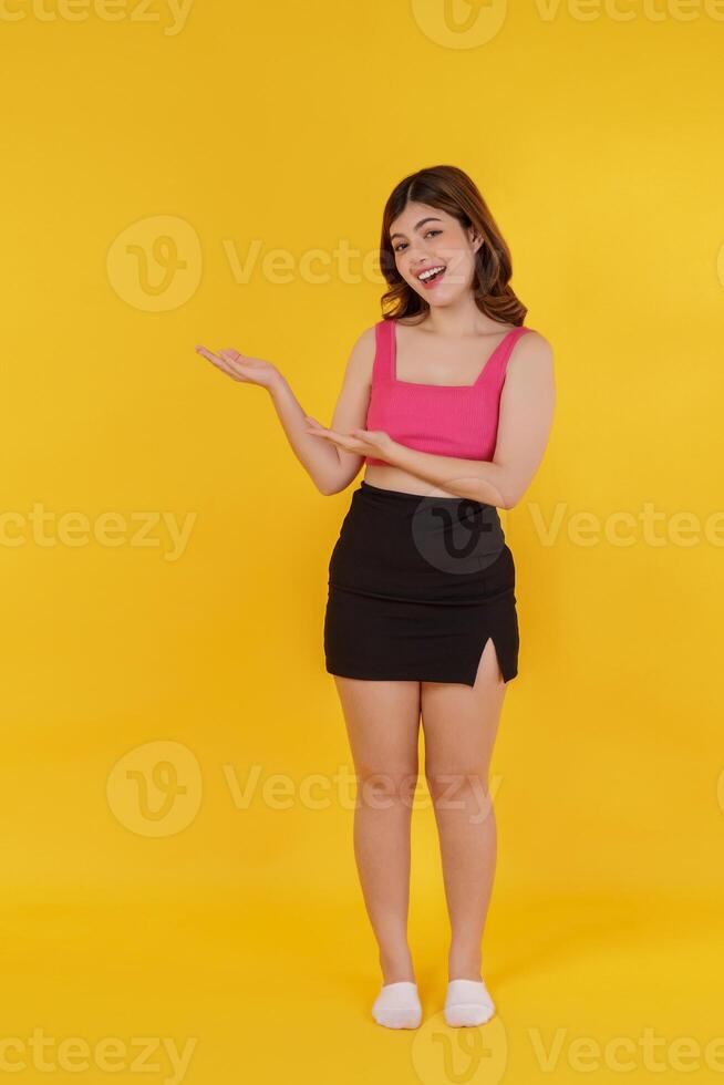 Portrait of Surprised young woman presenting or showing open hand palm with copy space for product over isolated yellow background photo