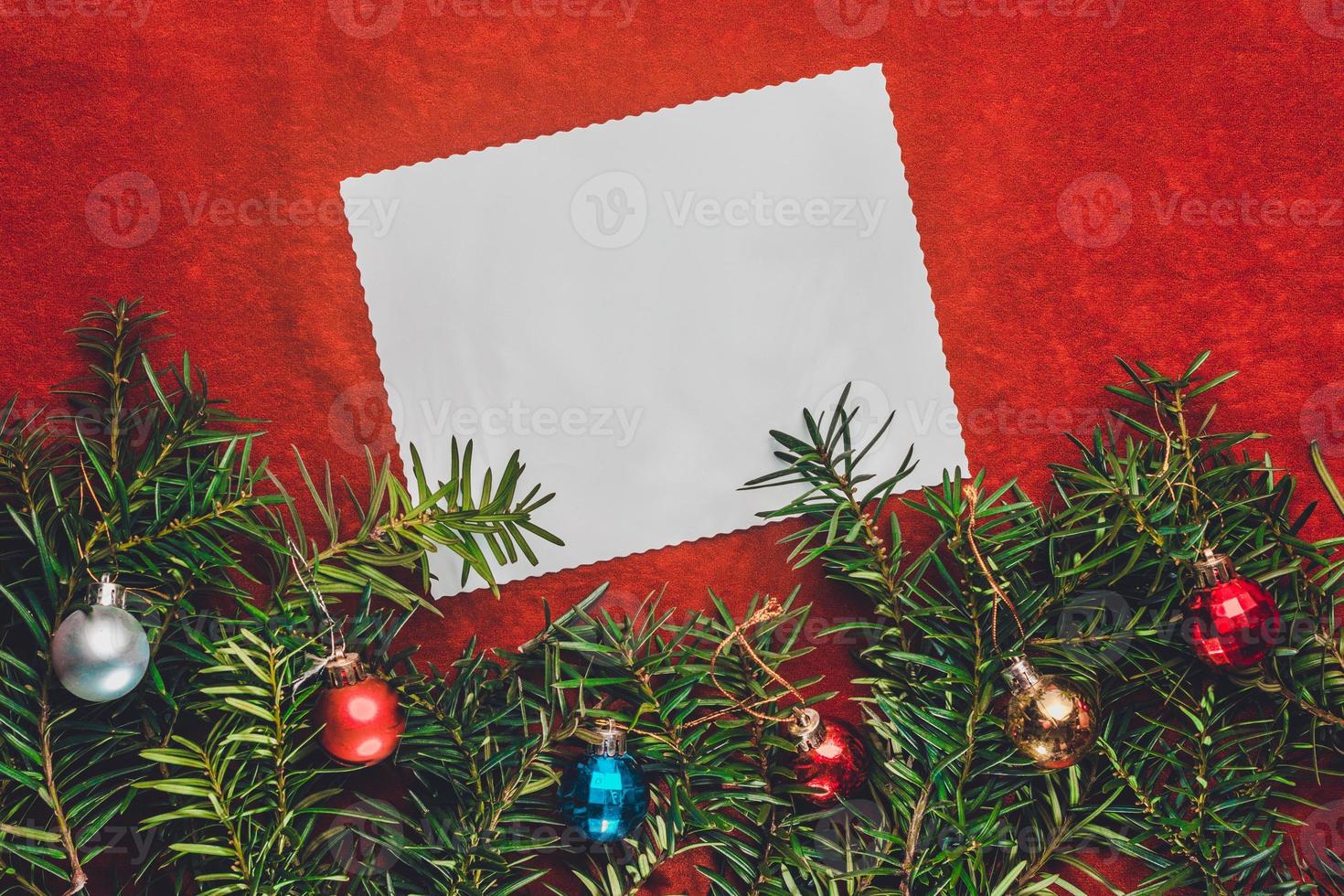 trozo de papel para deseos de navidad sobre un fondo rojo con ramas de árbol de navidad y bolas de navidad. foto