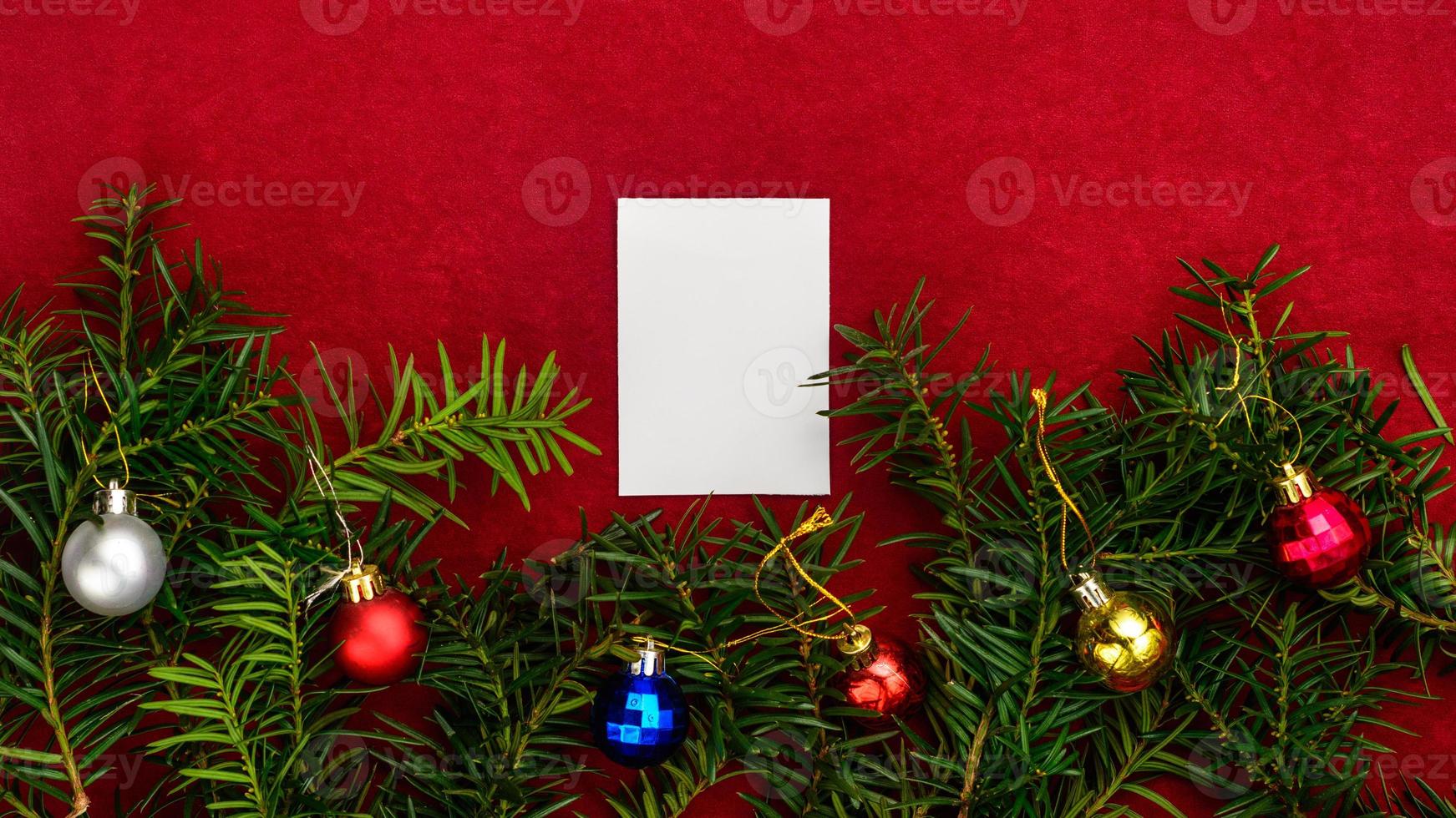 Piece of paper for Christmas wishes on a red background with branches of Christmas tree and Christmas balls. photo