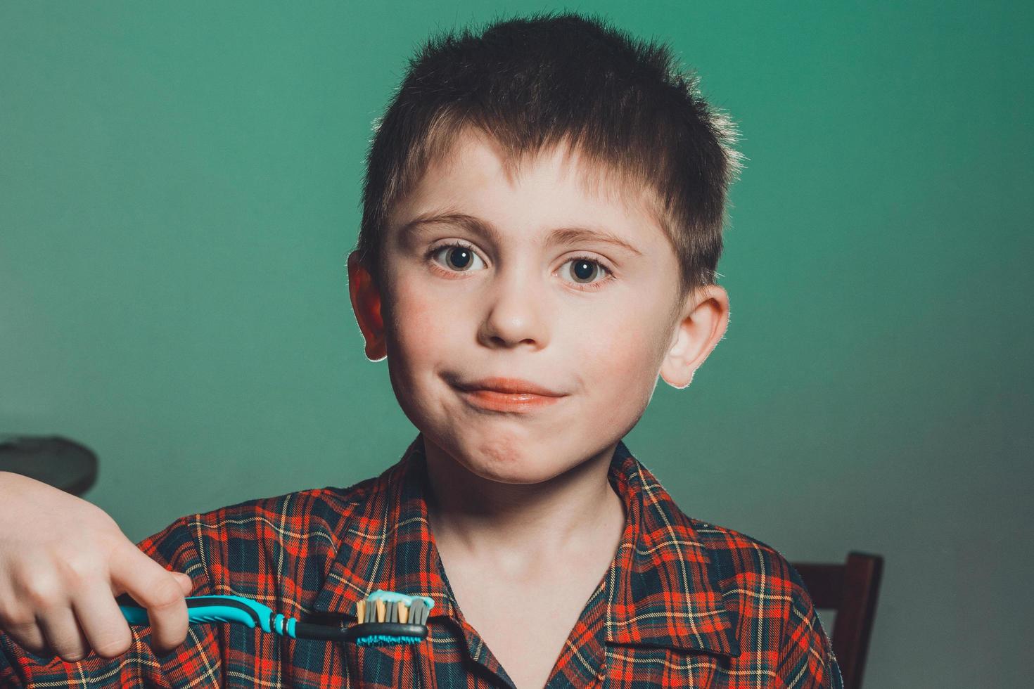A beautiful little boy in a pajamas smiles and holds in his hand a toothbrush on a greenbackground photo