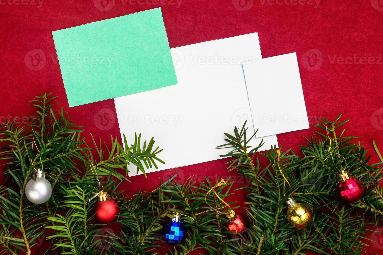 Piece of paper for Christmas wishes on a red background with branches of Christmas tree and Christmas balls. photo