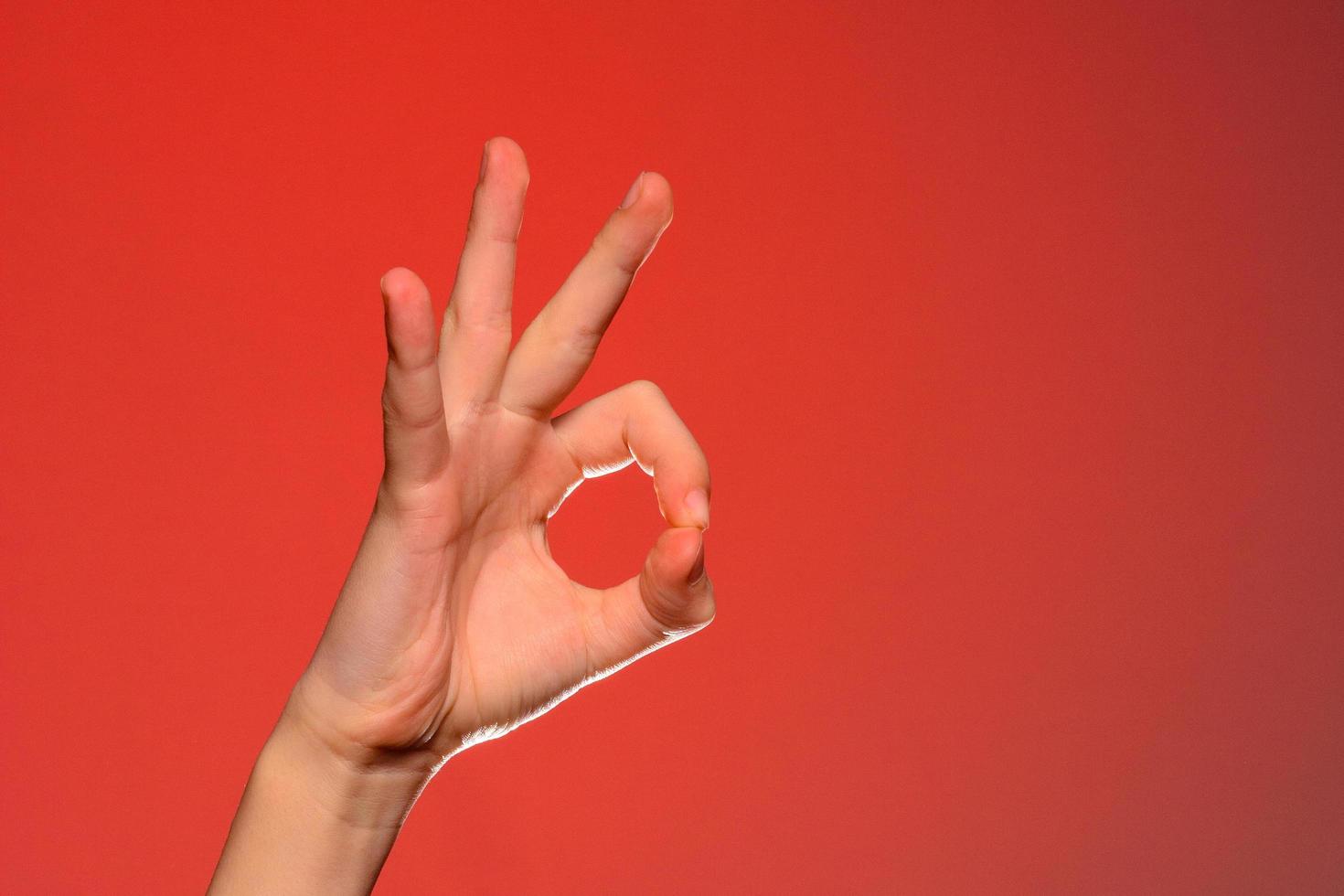 la mano humana muestra el signo ok que simboliza lo positivo, aislado en un fondo rojo. foto