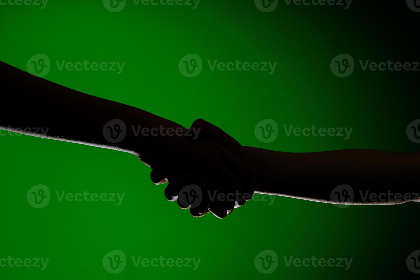 Two hands handshake, isolated on a green background, symbolizing friendship and reconciliation photo