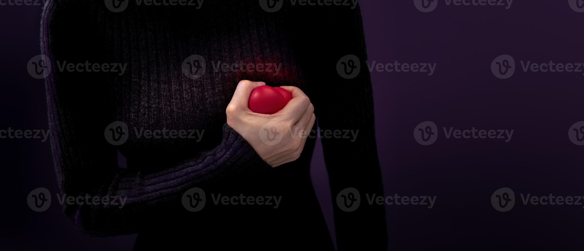 Painful, Heart Attack Concept. Young Woman Squeezed a Red Plastic Heart against her Chest. Heart Disease or feeling very Heartbreak and Sorrow photo