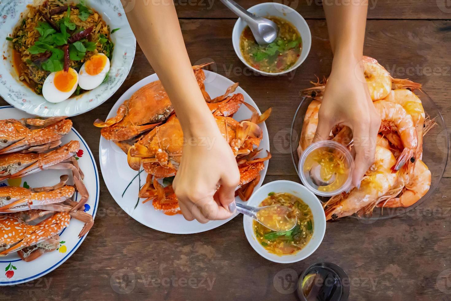 Top view Steamed Crabs and Shrimps set on the vintage wooden table with the the Asian hand picks up seafood sauce above of it before they eat. photo