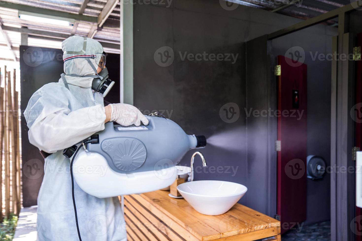 técnico profesional con traje de prevención con su máquina esterilizadora y aerosoles de agua desinfectantes en el baño o en el área de wc para purificar el coronavirus foto