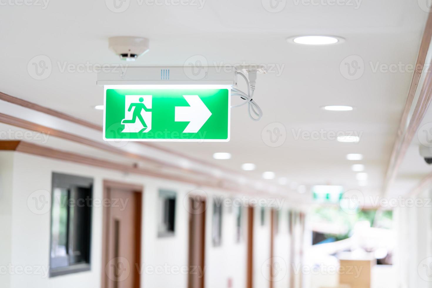 A Arrow light box sign of EMERGENCY FIRE EXIT is hung on the ceiling in hospital walkway, Idea for event fire or evacuation drills. photo