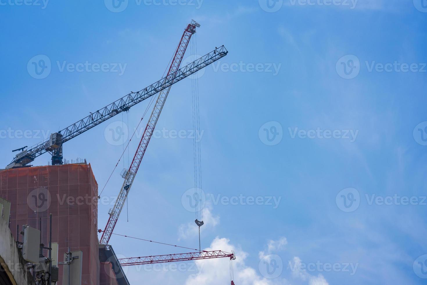 3 jib cranes settl on the building is moving to construct incompleted building with hook and cable hang on to it. photo
