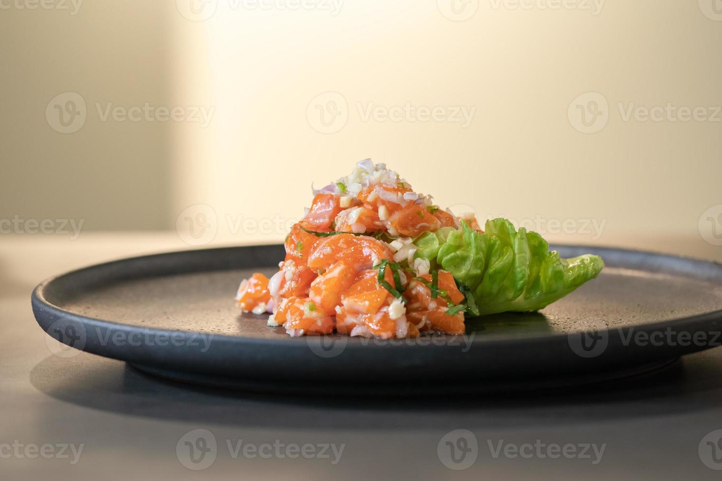 ensalada picante de salmón crudo al estilo de comida tailandesa decorada con piel de pescado frito crujiente y flor amarilla encima y microhierba alrededor del plato. listo para servir y comer. foto