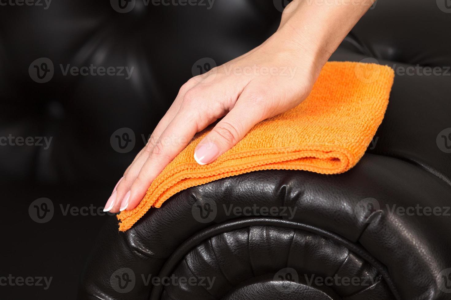 Closeup shot of female hand with beautiful manicured fingers wiping brown leather couch photo