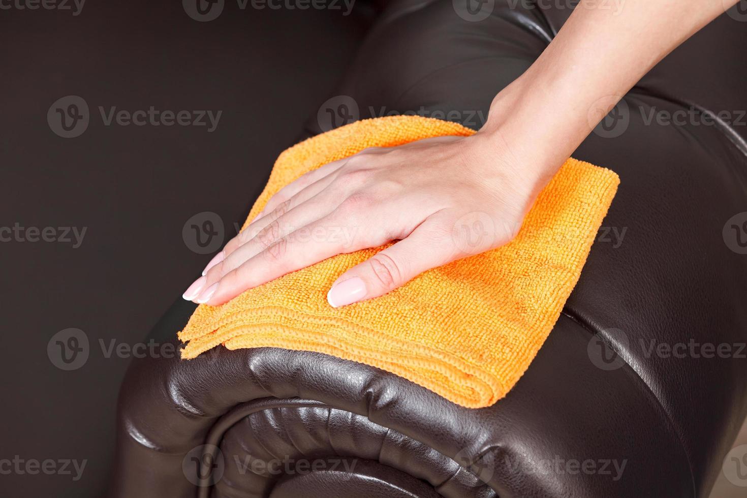 Closeup shot of female hand wiping brown leather chester couch or sofa photo