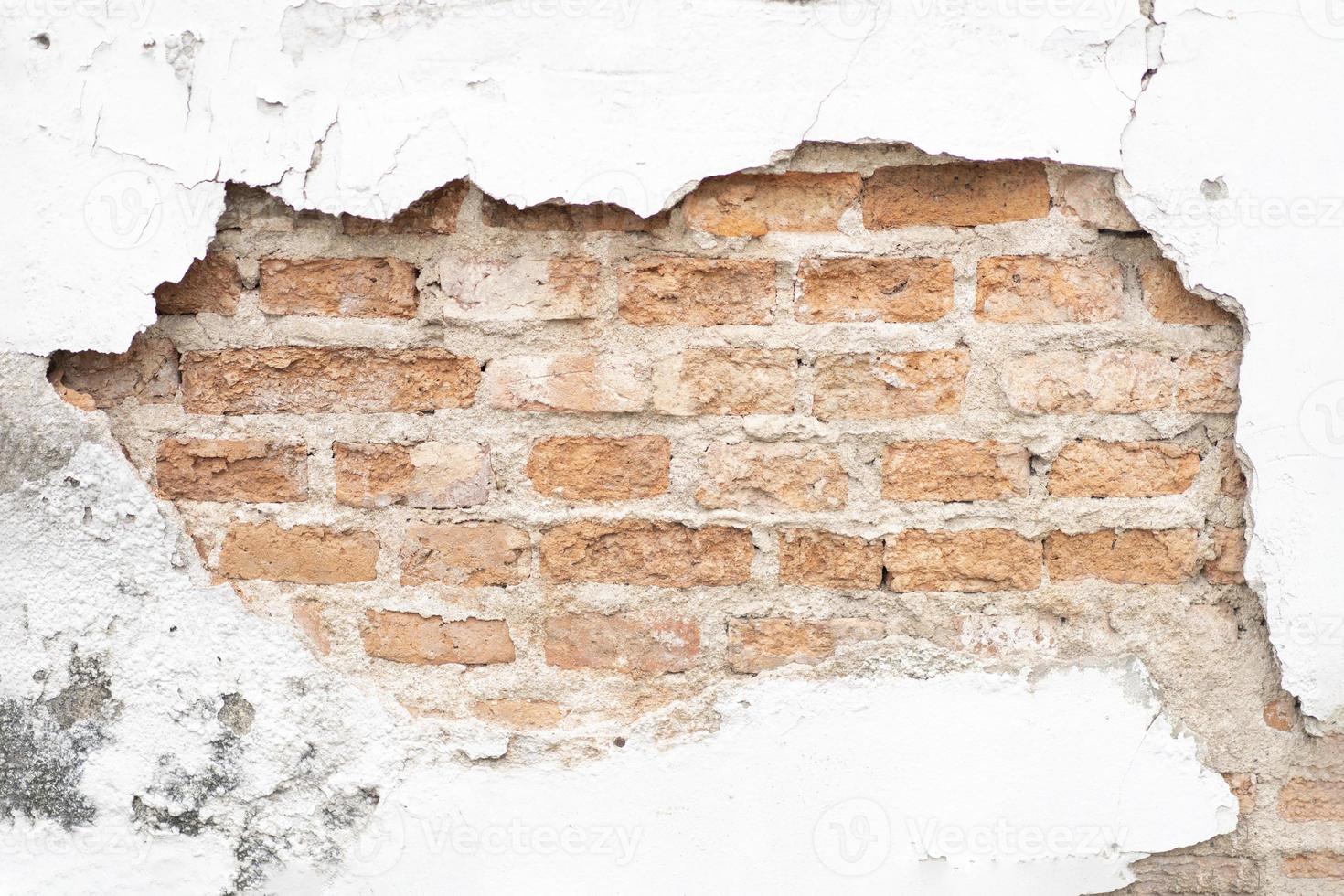 pared de superficie de cemento blanco agrietada y rota en el exterior que muestra el patrón de la pared de ladrillo en su interior foto