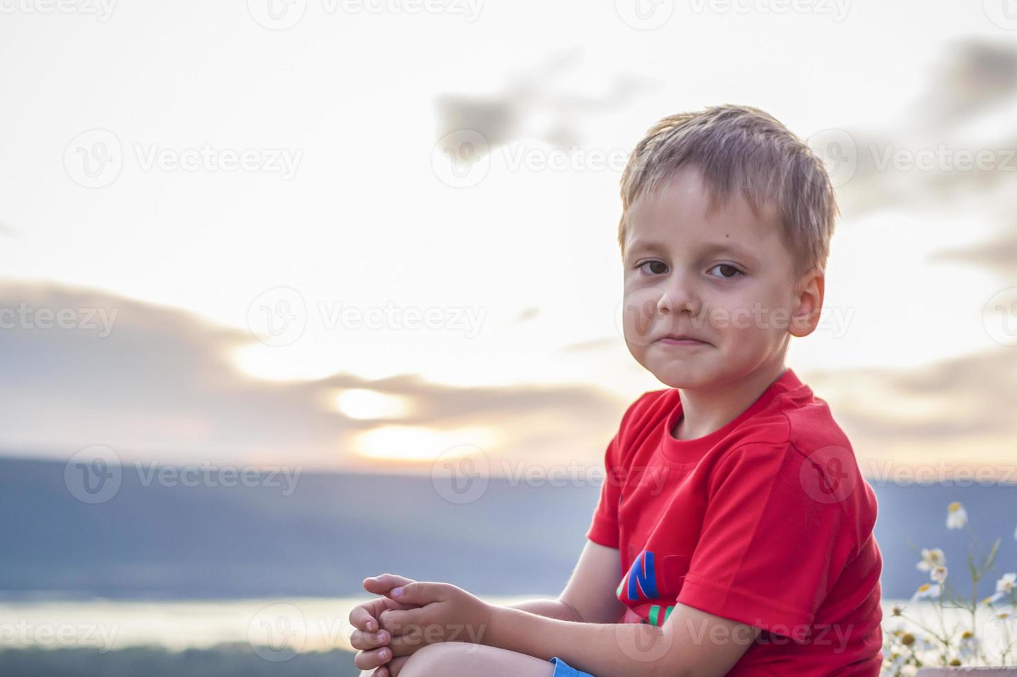 Cute Boy in a red T-shirt on the background of a stunning sunset. Journey.  The face expresses natural joyful emotions. Not staged photos from nature.