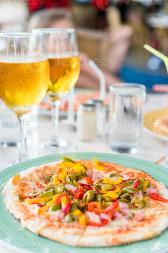 pizza con queso mozzarella, aceitunas, tomate fresco y salsa pesto. servido en la mesa del restaurante con dos cervezas foto