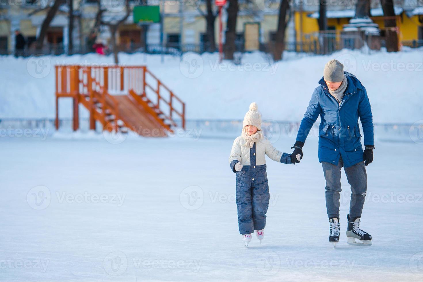 adorable niña con padre aprendiendo a patinar en la pista de hielo foto