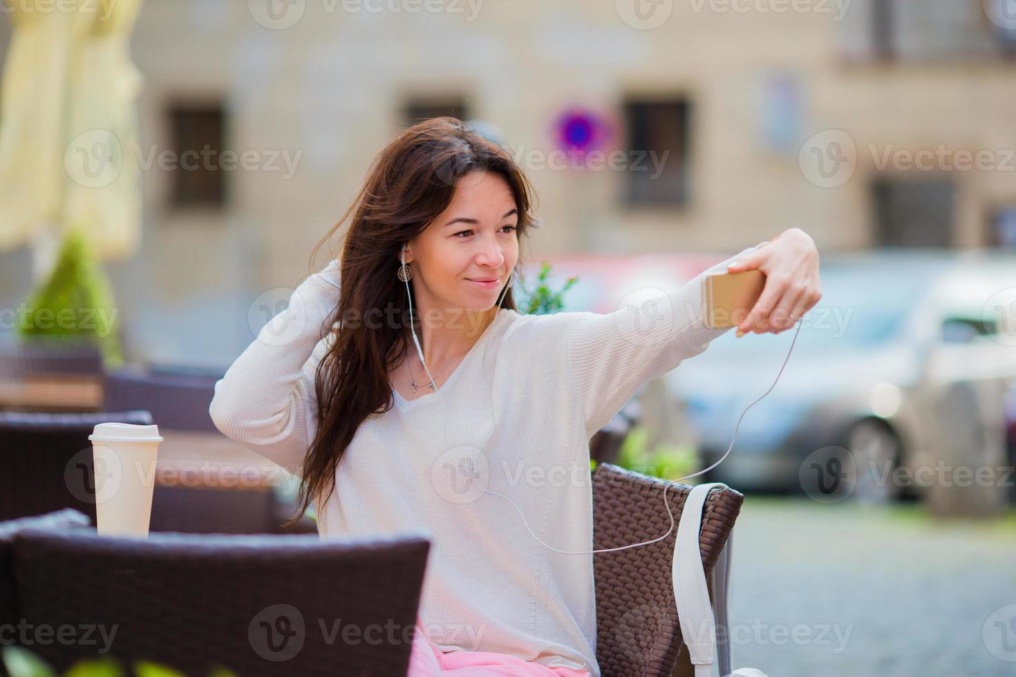 Young caucasian woman sending message and taking self portrait in outdoor cafe photo