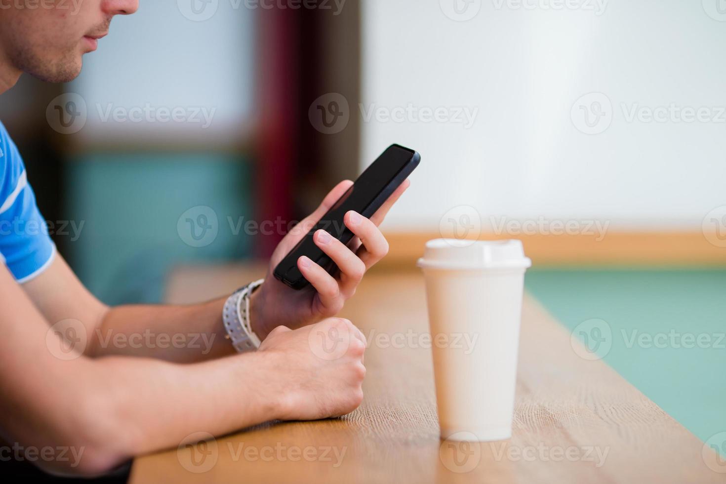 Closeup of male hands holding cellphone and class of cofee in cafe. Man using mobile smartphone photo