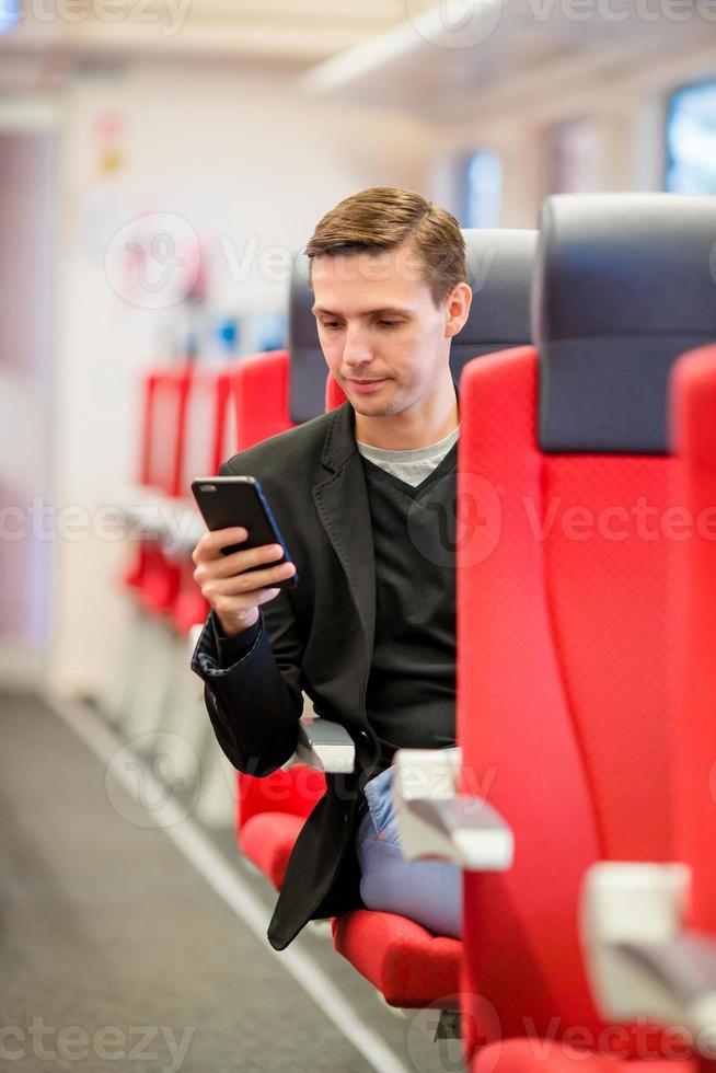 Young happy man traveling by train. Tourist writing a message on cellphone while traveling by express train photo