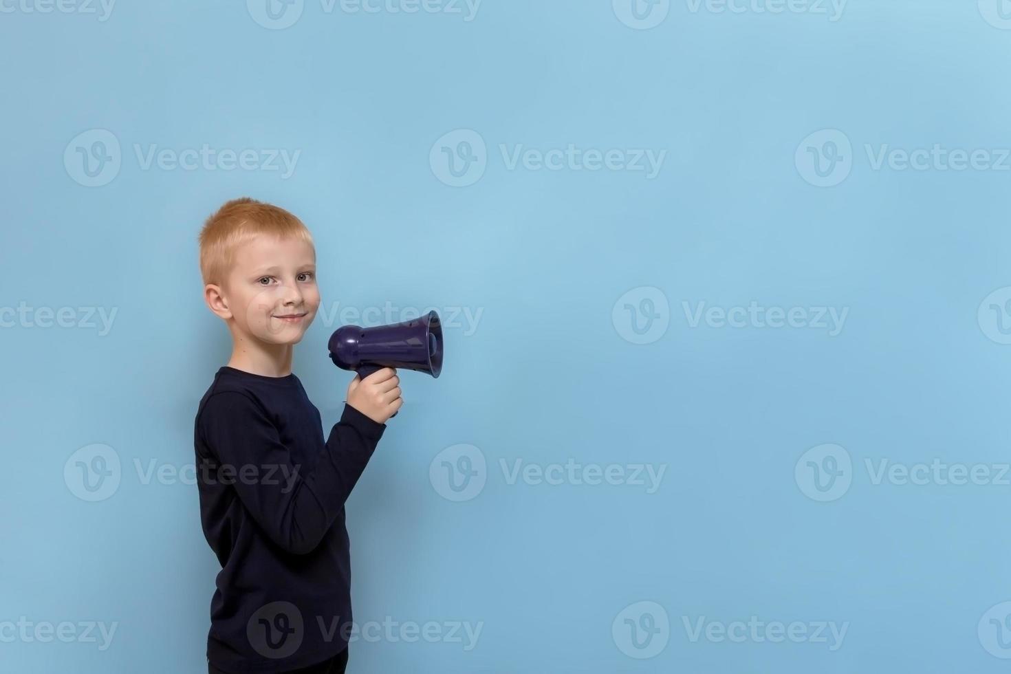 cute blond boy with megaphone smiling on blue background with copy space photo