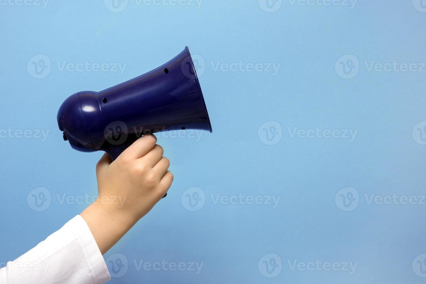 children's hand with a toy megaphone on a blue background with copy space photo