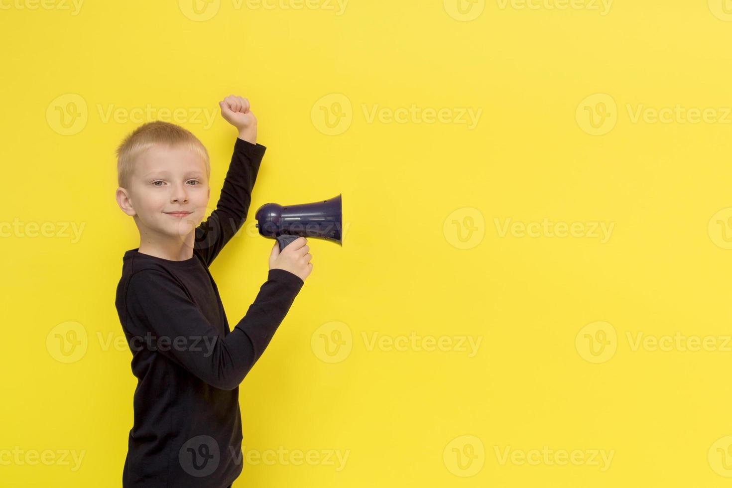 boy with a triumphant look holds a bullhorn in his hand, the second hand is raised and clenched into a fist on a yellow background with copy space photo